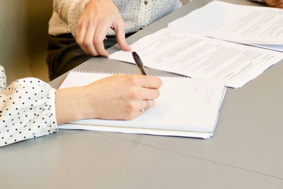 woman signing on white printer paper beside woman about to touch the documents