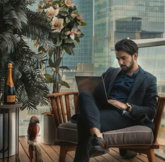 A man in a suit using a laptop on a balcony with city skyscrapers